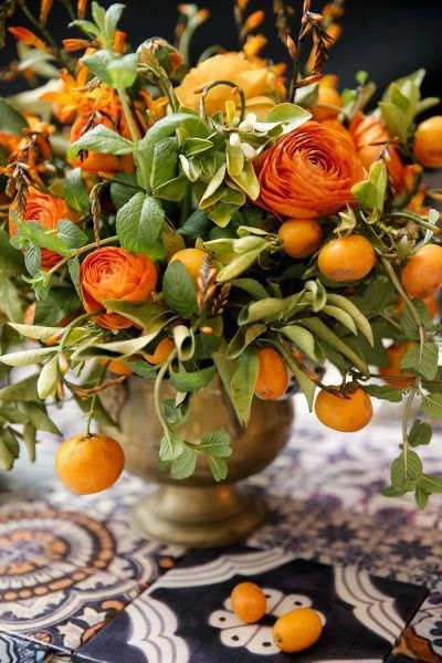 Fall centerpiece of persimmons and orange ranunculas in a silver, footed container.